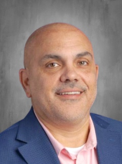 Dr. Daniel Nerelli is wearing a blue business suit with a collared shirt.